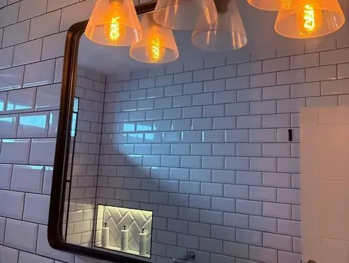 A mirror reflecting a lit tiled bathroom niche, framed by white subway tile