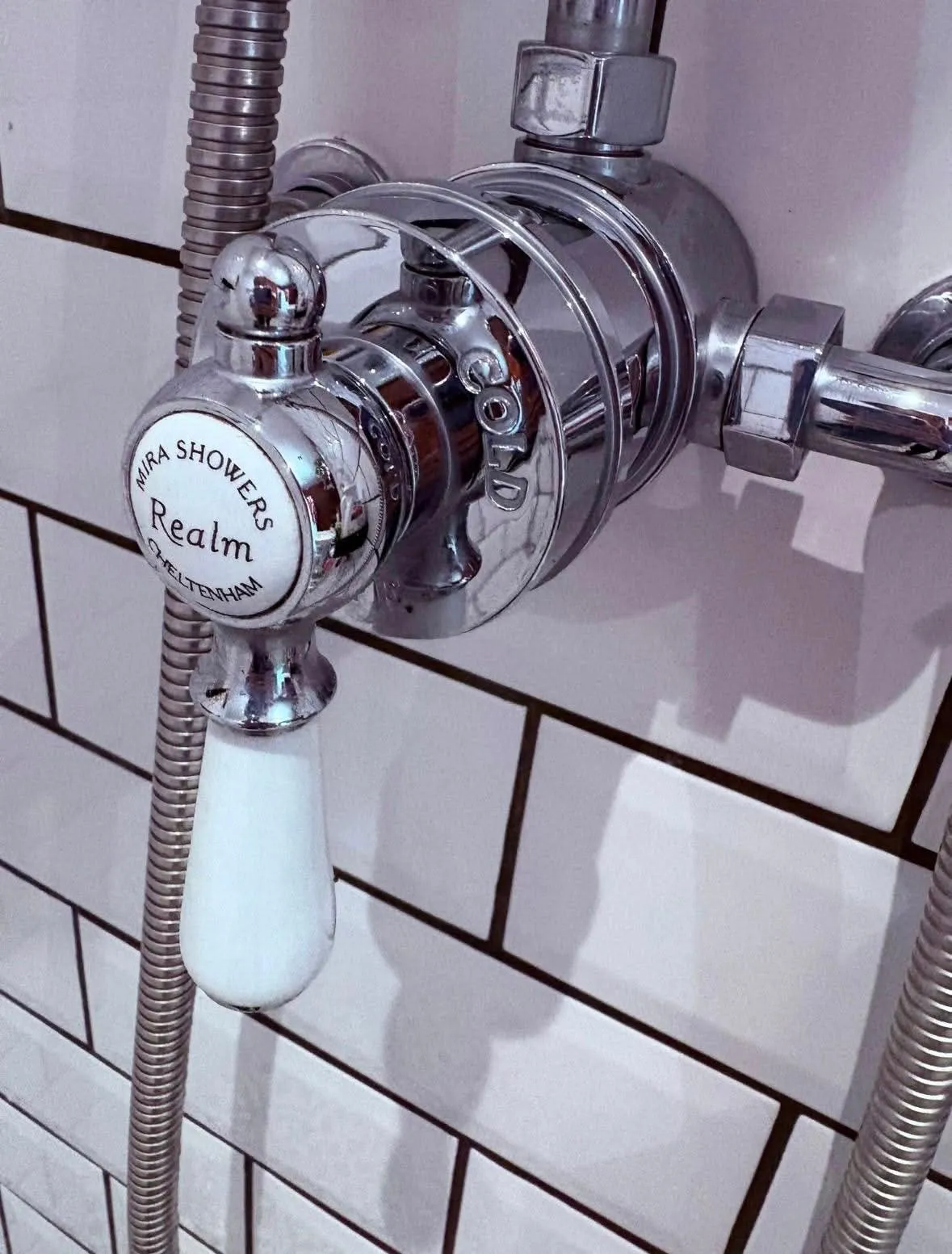 A polished chrome shower mixer valve against crisp white tiling