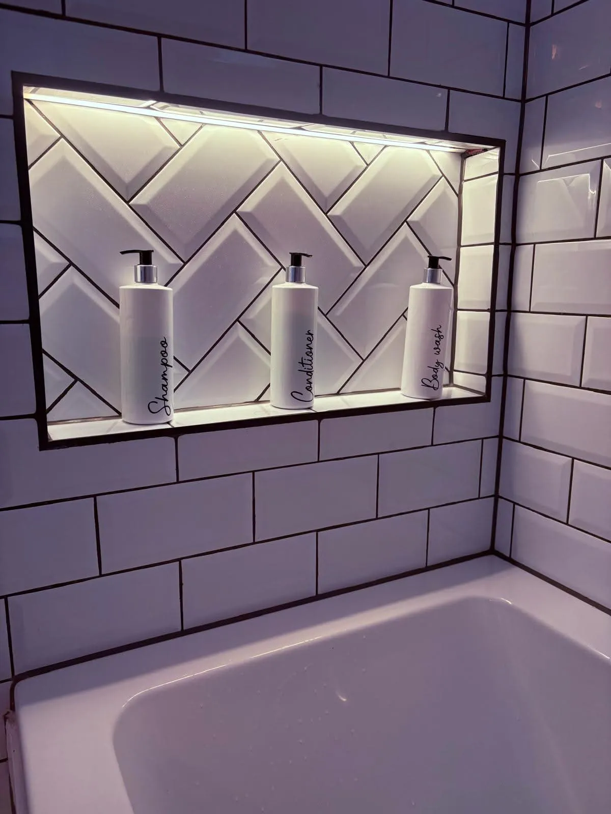 Lit recessed bathroom shelf with shampoo, conditioner and body wash, guest-ready
