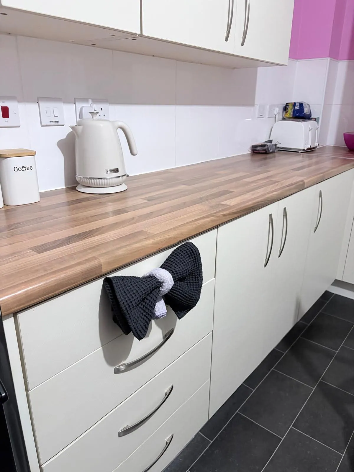 A spotless kitchen counter with kettle, and a black tea towel tied in a bow below